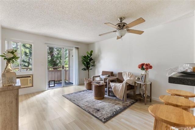 living area with a textured ceiling, cooling unit, light wood-style flooring, a ceiling fan, and baseboards