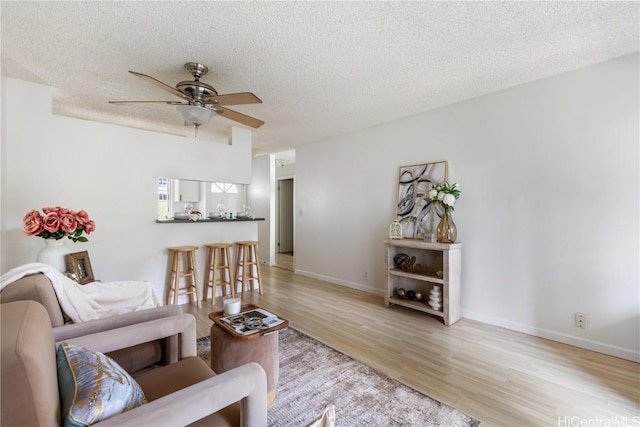 living room featuring a textured ceiling, light wood-type flooring, a ceiling fan, and baseboards