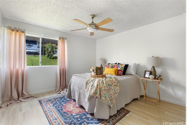 bedroom with a textured ceiling, ceiling fan, light wood-type flooring, and baseboards