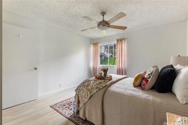 bedroom with light wood-style floors, baseboards, a ceiling fan, and a textured ceiling