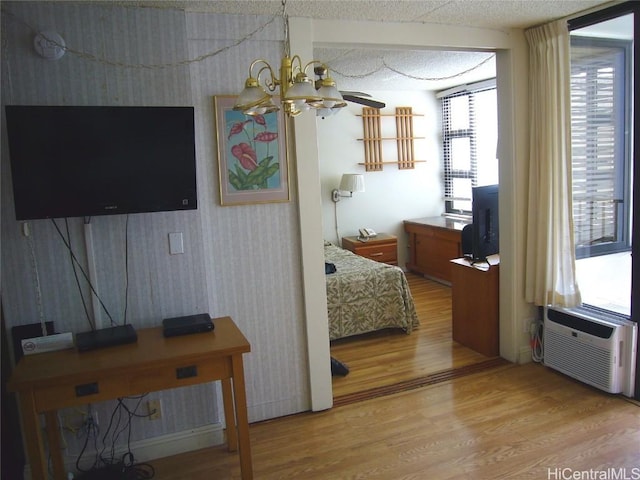 bedroom with light wood finished floors, an inviting chandelier, and a wall mounted AC