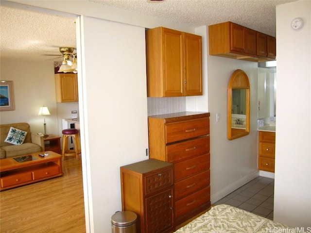 kitchen featuring a textured ceiling, light tile patterned floors, a ceiling fan, baseboards, and brown cabinetry