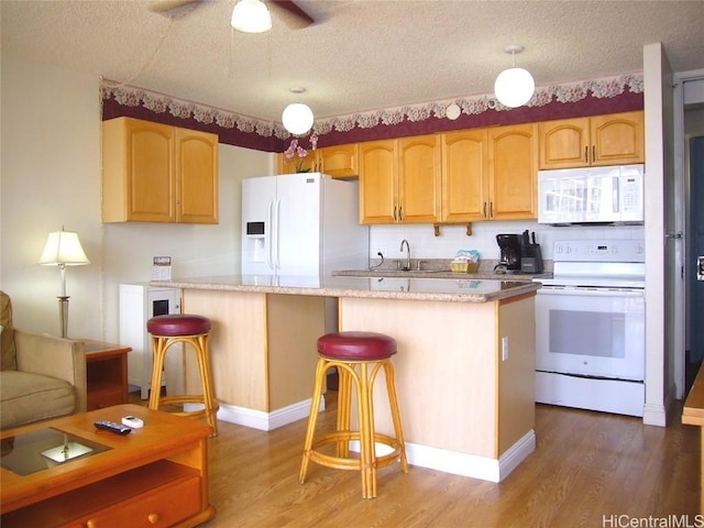 kitchen with white appliances, a kitchen bar, wood finished floors, and a textured ceiling