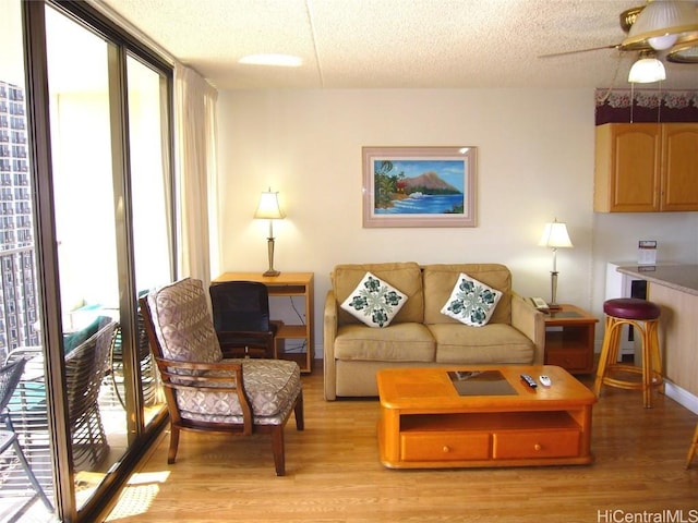 living area with floor to ceiling windows, a ceiling fan, a textured ceiling, light wood-type flooring, and baseboards