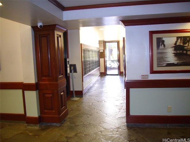 hallway with ornamental molding, stone tile flooring, and baseboards