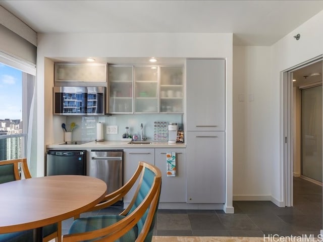 kitchen with light countertops, stainless steel microwave, backsplash, a sink, and dishwasher