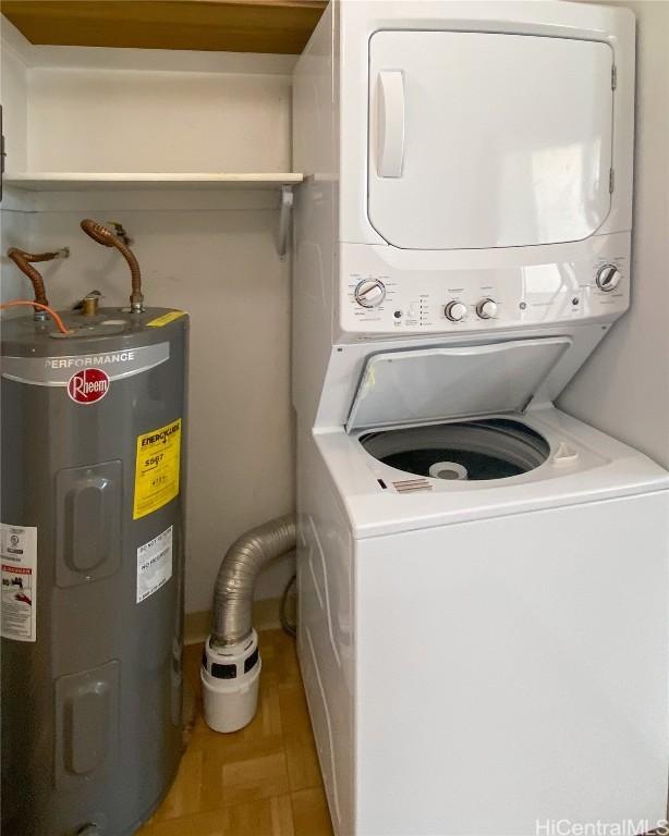 clothes washing area featuring stacked washer / dryer, water heater, and wood finished floors