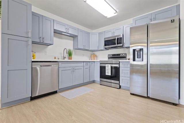 kitchen with appliances with stainless steel finishes, light wood-style floors, light countertops, and a sink