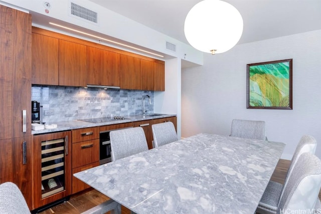 kitchen featuring black electric cooktop, beverage cooler, visible vents, and brown cabinetry