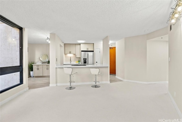 kitchen featuring a breakfast bar area, light countertops, light colored carpet, a textured ceiling, and stainless steel fridge with ice dispenser