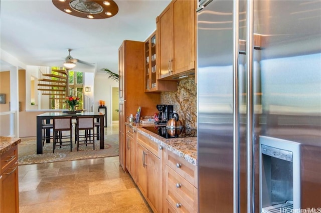 kitchen with high end refrigerator, decorative backsplash, glass insert cabinets, brown cabinets, and black electric stovetop