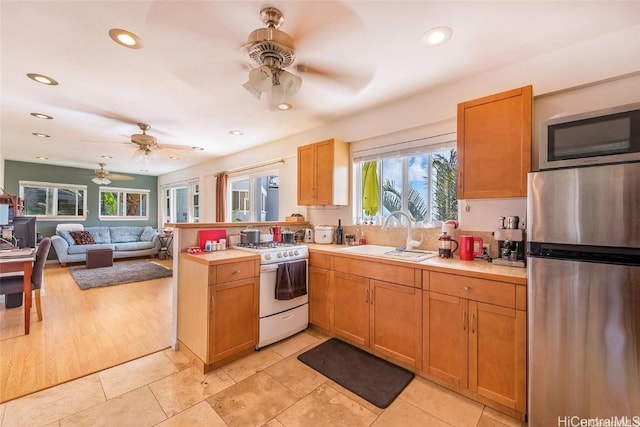 kitchen with stainless steel appliances, a peninsula, a sink, open floor plan, and light countertops