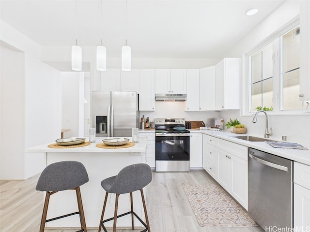 kitchen with under cabinet range hood, a sink, appliances with stainless steel finishes, light wood finished floors, and a kitchen bar