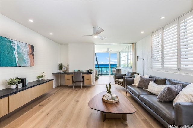 living area with a ceiling fan, a wall of windows, light wood-style floors, built in desk, and recessed lighting