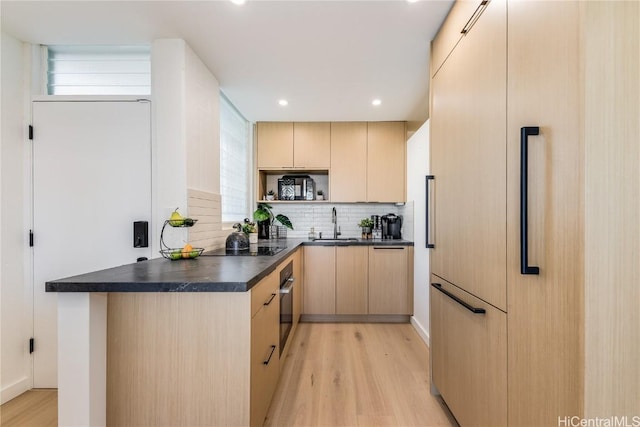 kitchen with dark countertops, light wood-style floors, paneled fridge, and light brown cabinetry