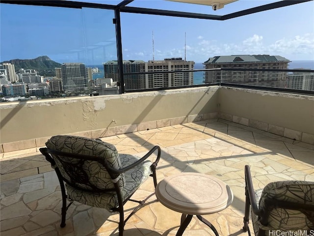 view of patio with a view of city, glass enclosure, and a balcony