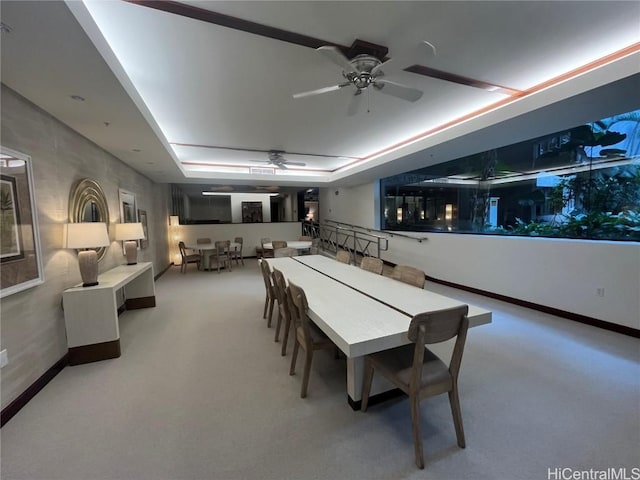 carpeted dining room with a tray ceiling, a ceiling fan, and baseboards