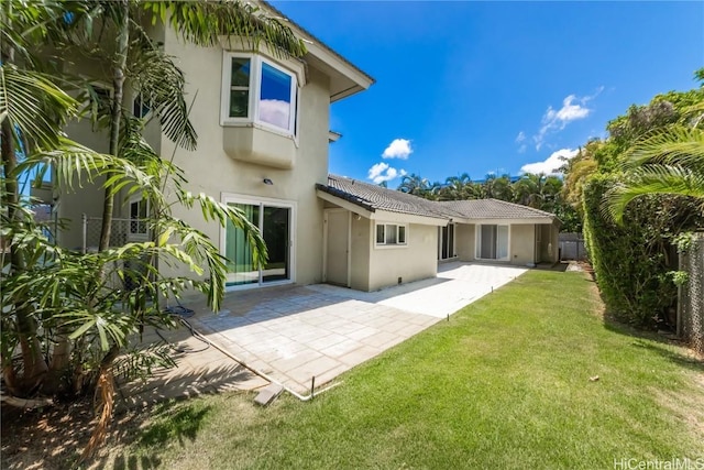 rear view of house featuring a patio, a tile roof, fence, a yard, and stucco siding