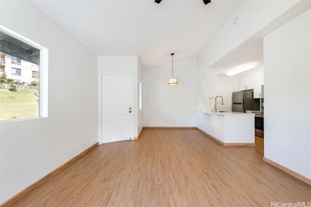 unfurnished living room featuring lofted ceiling, light wood-type flooring, and baseboards