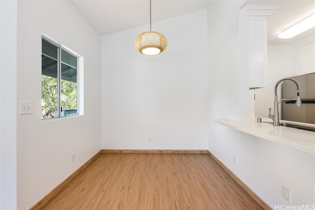 unfurnished dining area featuring baseboards, a sink, and light wood finished floors