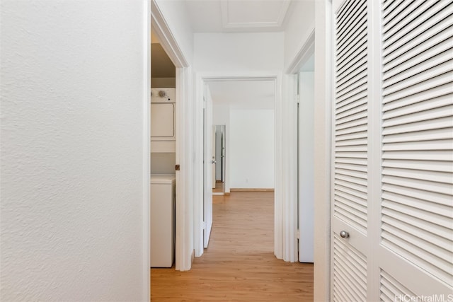 hallway with stacked washer and dryer, a textured wall, and light wood finished floors