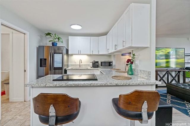 kitchen with appliances with stainless steel finishes, white cabinetry, a sink, light stone countertops, and a peninsula