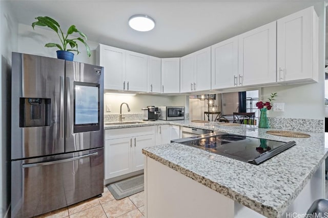 kitchen with light tile patterned floors, a peninsula, stainless steel appliances, white cabinetry, and a sink