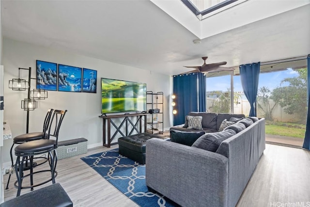 living area with a skylight, a ceiling fan, baseboards, and wood finished floors