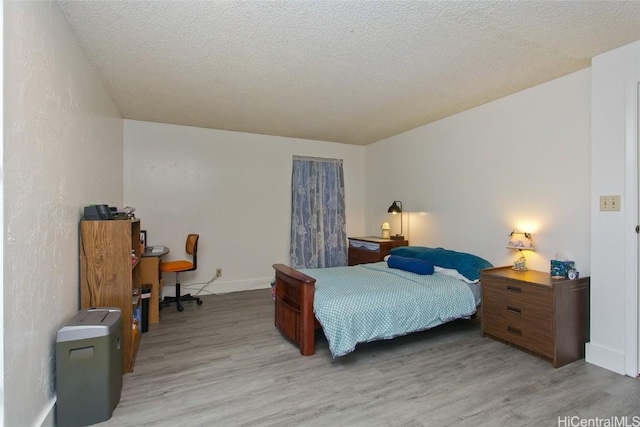 bedroom featuring a textured ceiling, light wood-style flooring, and baseboards