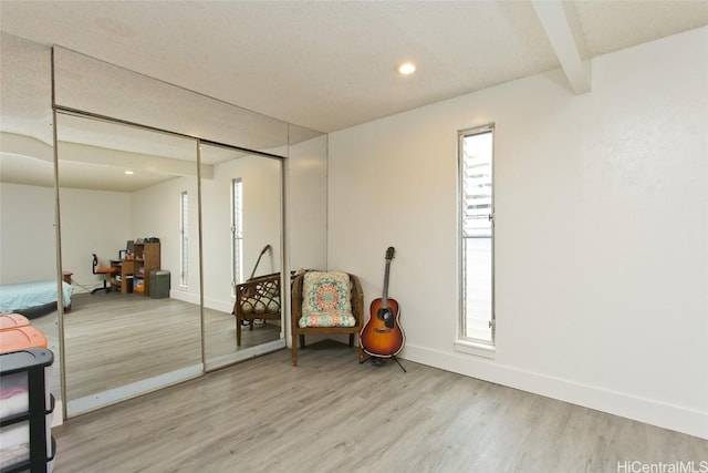 living area featuring a wealth of natural light, baseboards, beamed ceiling, and light wood finished floors