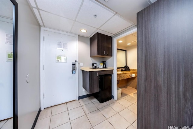 kitchen with dark brown cabinetry, light countertops, a paneled ceiling, built in desk, and light tile patterned flooring