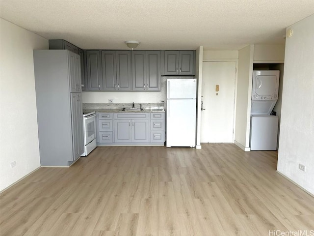 kitchen with light wood-style floors, white appliances, light countertops, and stacked washing maching and dryer