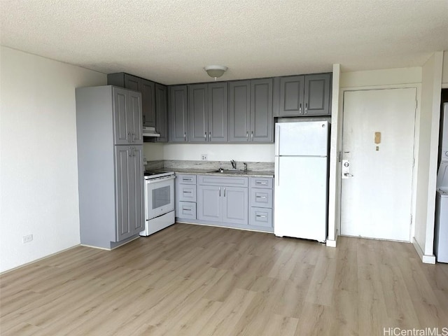 kitchen featuring gray cabinetry, light wood-style floors, a sink, white appliances, and under cabinet range hood