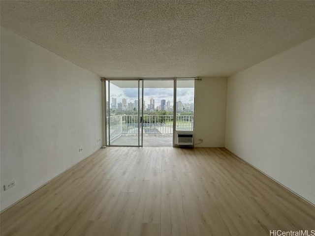 unfurnished room with a textured ceiling, light wood finished floors, a wall of windows, and a city view