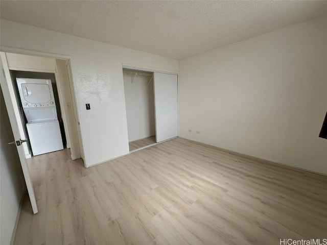 unfurnished bedroom featuring light wood-style floors, stacked washer / drying machine, a closet, and a textured ceiling