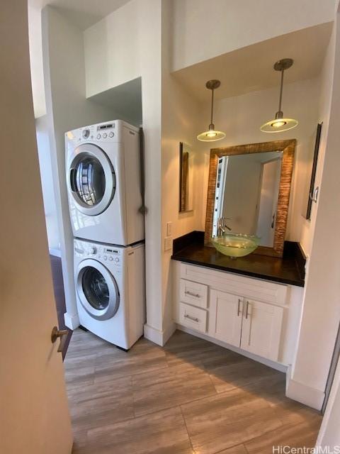 laundry area featuring laundry area, stacked washer and clothes dryer, light wood-style floors, and a sink