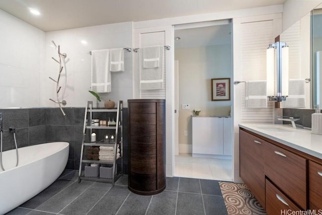 bathroom with tile walls, a freestanding bath, vanity, and tile patterned floors