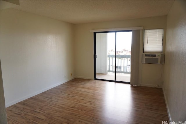 empty room featuring a textured ceiling, wood finished floors, cooling unit, and baseboards