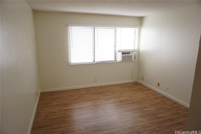 unfurnished room with a textured ceiling, cooling unit, wood finished floors, and baseboards