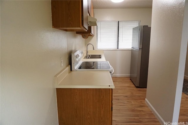 kitchen with electric range, a sink, baseboards, light wood-type flooring, and freestanding refrigerator