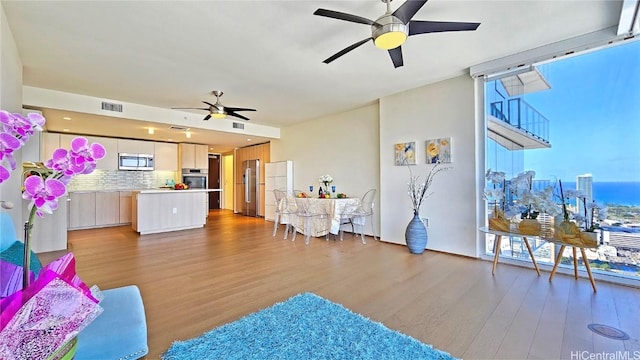 living area with expansive windows, visible vents, ceiling fan, and wood finished floors