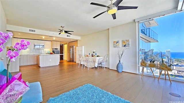 living room featuring expansive windows, visible vents, ceiling fan, and light wood-style flooring