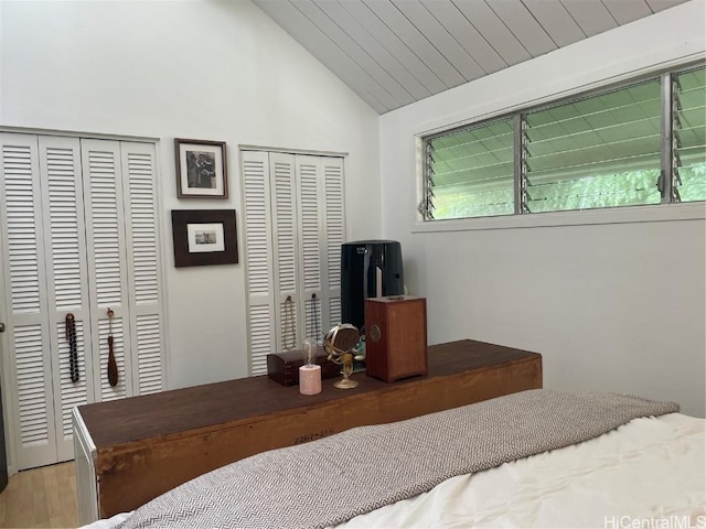 bedroom featuring light wood-type flooring, wooden ceiling, vaulted ceiling, and two closets