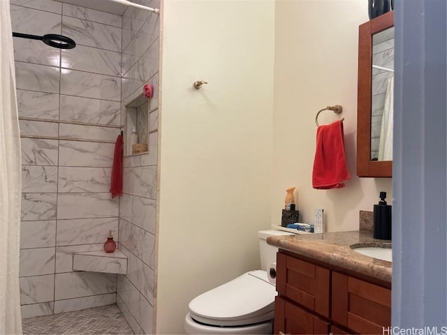 bathroom with toilet, tiled shower, and vanity