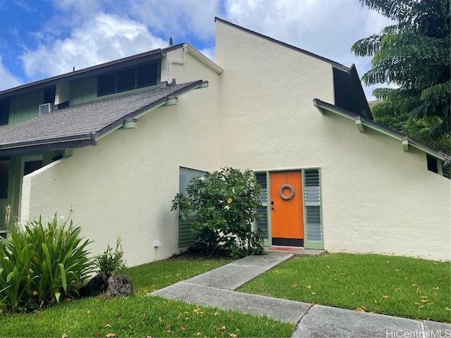 view of front of home with stucco siding, a front yard, and roof with shingles