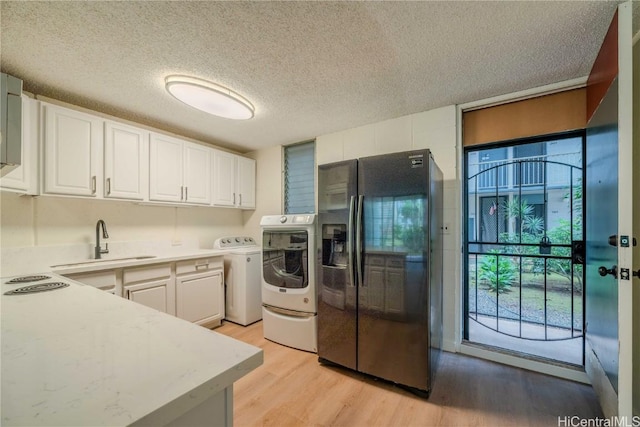 kitchen with black fridge with ice dispenser, light wood-type flooring, washing machine and dryer, white cabinetry, and a sink