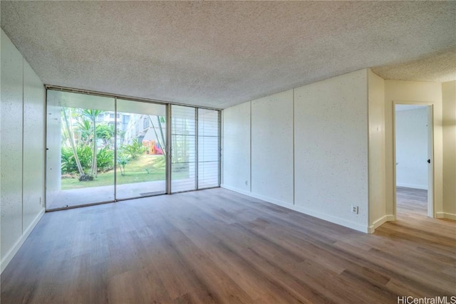 empty room featuring baseboards, a textured ceiling, floor to ceiling windows, and wood finished floors