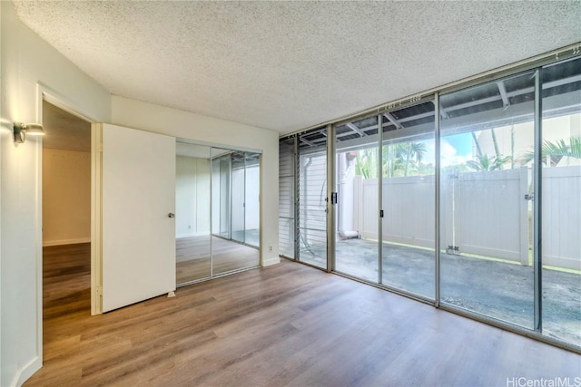 empty room featuring a textured ceiling, a wall of windows, wood finished floors, and baseboards