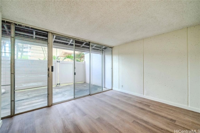 empty room featuring expansive windows, a textured ceiling, baseboards, and wood finished floors