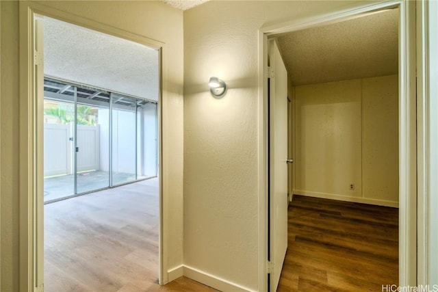 hallway with baseboards, wood finished floors, and a textured wall